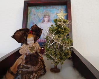 May include: A miniature Christmas scene in a wooden box. It features a doll with a large brown bow, a small Christmas tree with a star, and a framed image of a fairy. The background includes the text "FAIRY CHRISTMAS BOX".
