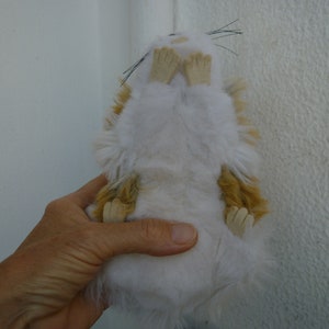 May include: A white and brown plush toy hamster with black eyes and whiskers. The hamster is lying on its back with its paws in the air.