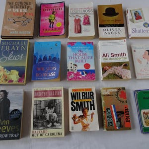 Puede incluir: Una colección de libros de tapa dura con varios títulos y autores, incluyendo "The Curious Incident of the Dog in the Night-Time" y "Skios". Los libros están dispuestos sobre una superficie blanca, mostrando sus coloridas portadas.