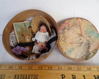 Puede incluir: Una caja de madera vintage con una muñeca, accesorios en miniatura y una postal. La muñeca viste un vestido blanco y un sombrero de paja. La tapa de la caja presenta una escena pastoral con un unicornio. La caja tiene unos 15 cm de diámetro.