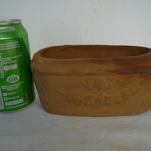 Può includere: Una fioriera rettangolare in terracotta non smaltata. La fioriera ha un bordo leggermente rialzato e una superficie strutturata. Una lattina verde di Sprite è accanto alla fioriera per il confronto delle dimensioni.