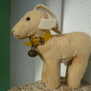 May include: A plush toy goat with a yellow collar and a bell. The goat is light brown with white fur on its ears.