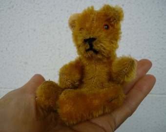 Puede incluir: Un pequeño oso de peluche marrón con ojos negros y nariz negra. El oso está sentado en la palma de una mano.