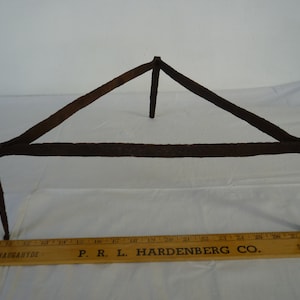 May include: A rustic, triangular metal stand with three legs. The stand is made of iron and has a dark brown patina. It is approximately 61 cm wide.