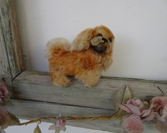 Pode incluir: Um cão de pelúcia vintage com pelo marrom, sentado em uma prateleira de madeira. O cão tem um focinho curto e orelhas caídas.