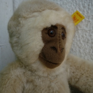 May include: A white plush monkey with a brown face and a yellow tag that says "Steiff" on it.