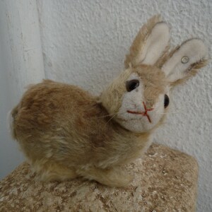 May include: A plush brown rabbit toy with long ears and a white face. The rabbit has a button on one ear and red stitching around the nose.
