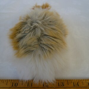 May include: A fluffy white and brown faux fur tail, approximately 12 inches long, with a white tip. The tail is lying on a wooden ruler.