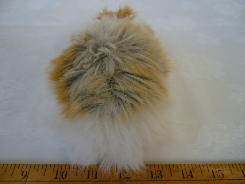 May include: A fluffy white and brown faux fur tail, approximately 12 inches long, with a white tip. The tail is lying on a wooden ruler.