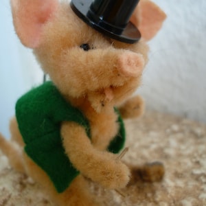 Puede incluir: Una encantadora figura de cerdo de estilo vintage con sombrero de copa y chaleco verde. El cerdo tiene un cuerpo marrón claro, orejas y hocico rosados, y sostiene un pequeño palo. Un objeto de colección artesanal y caprichoso.