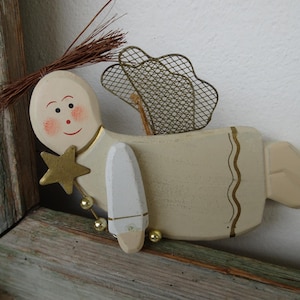 May include: A wooden angel ornament with a white painted finish and gold accents. The angel has a wire mesh halo and a star in its hand.