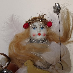 May include: A vintage angel figurine with a porcelain face, blonde hair, and red accents. The angel wears a white dress and holds a silver star on a wire. A small basket and a yellow lamb are also present.