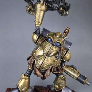 May include: A detailed figurine of a steampunk-inspired robot warrior. The figure is predominantly gold and bronze, with intricate mechanical details, blue eyes, and a weapon. It stands on a reddish-brown base, showcasing a blend of artistry and fantasy.