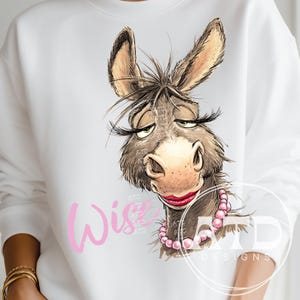 May include: White sweatshirt featuring a cartoon donkey with long eyelashes, red lipstick, and a pink pearl necklace. The word "Wise" is written in pink script. The design is by ATD Designs.