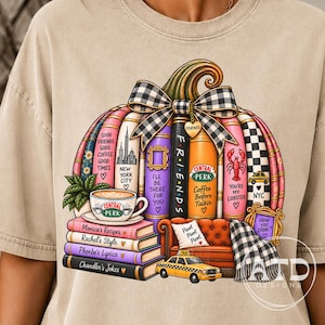 Könnte beinhalten: Ein beiges T-Shirt mit einer Grafik eines Kürbisses, der aus gestapelten Büchern und einer schwarz-weiß karierten Schleife besteht. Das Design enthält eine Central Perk Kaffeetasse, ein orangefarbenes Miniatursofa, ein gelbes Taxi und Textbezüge zur Serie Friends.