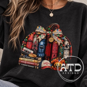 May include: A charcoal gray crewneck sweatshirt featuring a graphic of a pumpkin made of books, a cassette tape, a waffle, a baseball cap, and string lights. The books have titles like Friends Don't Lie, Hawkins Memories, and A Stronger Friendship.