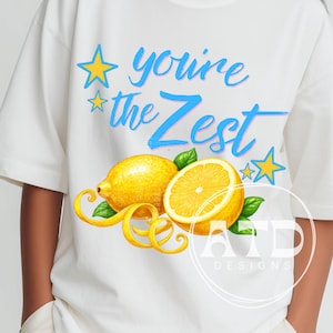 Può includere: T-shirt bianca con grafica di limone. Il design include due limoni, uno intero e uno a fette, con foglie verdi e scorza gialla. Il testo "you're the Zest" è in blu e rosa con stelle gialle.
