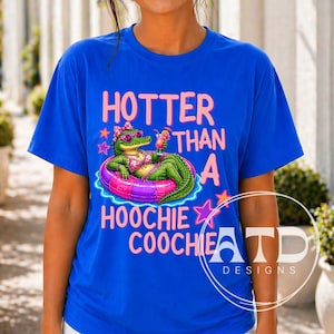 May include: Royal blue t-shirt with the text "HOTTER THAN A HOOCHIE COOCHIE" in pink. The graphic features an alligator in a pink bikini and sunglasses, floating on a pink and purple inner tube, holding a cocktail.