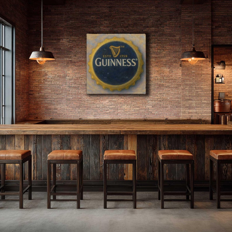 May include: A framed artwork featuring a Guinness bottle cap design, with a gold border and navy blue center, hangs on a brick wall. The bar setting includes a wooden counter, leather-topped stools, and pendant lights.