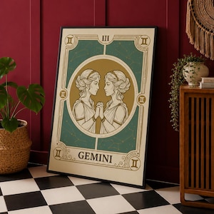 May include: Framed Gemini zodiac art print. The artwork features two women facing each other, holding hands, within a teal and gold circular design. The word "GEMINI" is at the bottom. The print is in a black frame, leaning against a red wall.