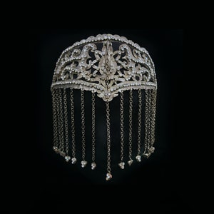 Może przedstawiać: Srebrna ozdoba głowy z misternymi wzorami kwiatowymi i zwisającymi łańcuchami. Ozdoba głowy jest ozdobiona małymi, przezroczystymi kryształkami.