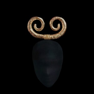May include: A black head-shaped sculpture with a gold-coloured, double-swirl design on top. The gold element is connected by a wrapped, gold-coloured band. The background is solid black.