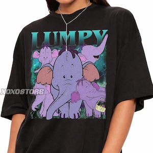 May include: Black t-shirt featuring a graphic of Lumpy the elephant and his friends from Winnie the Pooh. The word "LUMPY" is printed in teal above the elephant characters. The elephants are purple with brown ears and are set against a teal and green background.