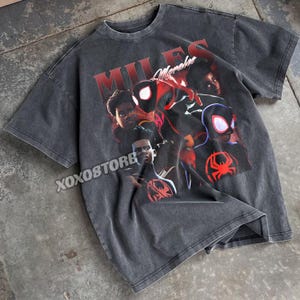 K&ouml;nnte beinhalten: Dunkelgraues T-Shirt mit einem Aufdruck von Miles Morales. Das Wort "MILES" ist rot gedruckt, mit "Morales" in Schreibschrift. Das T-Shirt hat einen Vintage-Look. Das Design zeigt mehrere Bilder der Figur.