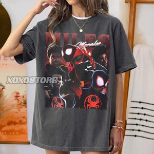 K&ouml;nnte beinhalten: Dunkelgraues T-Shirt mit einer Grafik von Miles Morales im Spider-Man-Anzug. Das Design enth&auml;lt den Text "MILES Morales" in Rot und Wei&szlig;. Das Shirt hat einen Vintage-Look.