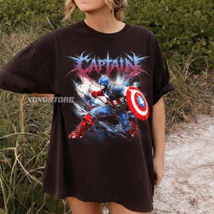 以下が含まれることがあります： キャプテン・アメリカが盾と武器を持ってアクションを起こしているグラフィックが特徴の濃い茶色のTシャツ。「CAPTAIN」の文字がキャラクターの上に様式化されたフォントで表示されています。シャツはヴィンテージで使い古された外観をしています。