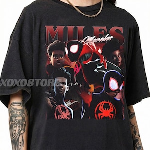 K&ouml;nnte beinhalten: Dunkelgraues T-Shirt mit einer Grafik von Miles Morales im Spider-Man-Anzug. Das Design enth&auml;lt den Namen "Miles Morales" in roter Schrift und mehrere Bilder der Figur. Das T-Shirt hat einen Rundhalsausschnitt und kurze &Auml;rmel.