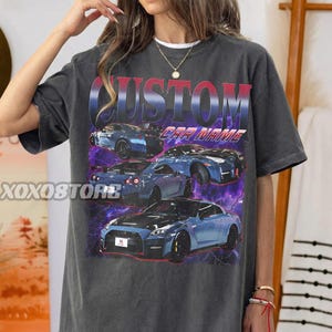 May include: Dark gray t-shirt featuring a graphic of several blue sports cars with a purple and white lightning effect. The word "CUSTOM" is printed in red and blue, with "CAR NAME" below. The brand name "XOXOSTORE" is printed on the left side.