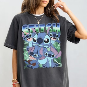 May include: A charcoal gray short-sleeve t-shirt featuring a graphic print of the character Stitch in various poses. The design includes the word STITCH in a blue and green gradient font, lightning bolts, and a small ice cream cone graphic.