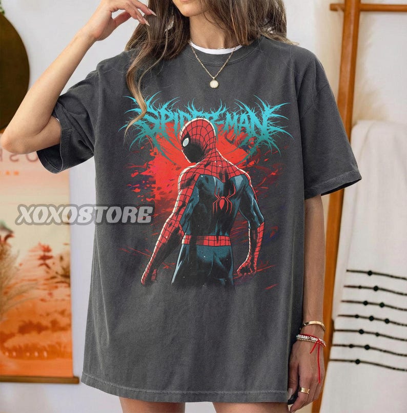 May include: Dark gray t-shirt featuring a graphic of Spider-Man from the back, with red and blue suit details. The text "SPIDER-MAN" is in blue, with a red background. The shirt has the text "XOXOSTORE" on the left side.