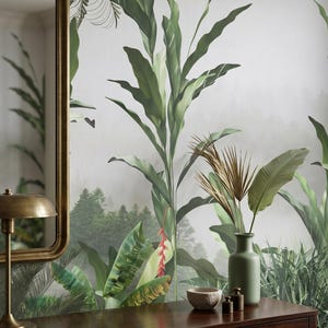 May include: A dark wood console table with a gold-framed mirror and a green vase holding dried leaves. The table displays a small stone bowl and two small decorative weights. The background features a tropical mural with lush green foliage.