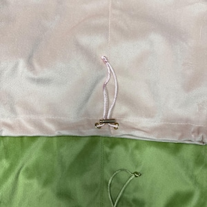 May include: Two velvet drawstring pouches, one in a soft pale pink and the other in a vibrant sage green. Each pouch features a matching thin fabric cord threaded through a metal eyelet, secured with a small, polished gold-tone metal toggle.