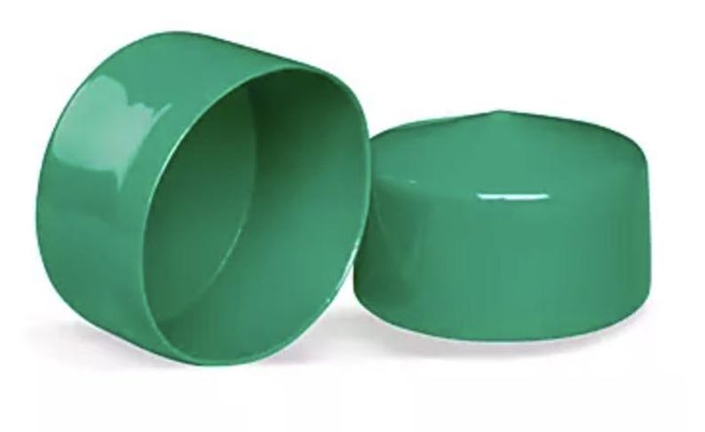 May include: Two smooth, cylindrical green plastic end caps. One cap is positioned on its side, revealing its hollow interior, while the other cap is placed upright, showing its solid, flat top surface. Both items feature a glossy finish.