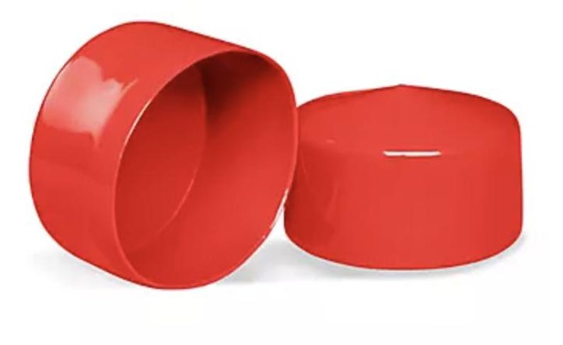 May include: Two bright red, cylindrical plastic end caps with a smooth, glossy finish. One cap is positioned to show its hollow interior, while the other is placed upside down to display its flat, solid top surface and rounded edges.