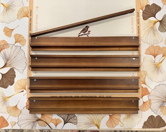 May include: Four rectangular wooden wall shelves with a dark brown finish, each featuring a horizontal groove for display. The shelves are arranged vertically, with one additional wooden strip placed diagonally across the top shelf.