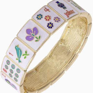 May include: A gold-toned bracelet featuring white rectangular tiles with colorful Mahjong symbols and a "Joker" tile. The tiles display various floral and bird designs, and the bracelet has a textured, brushed metal finish.
