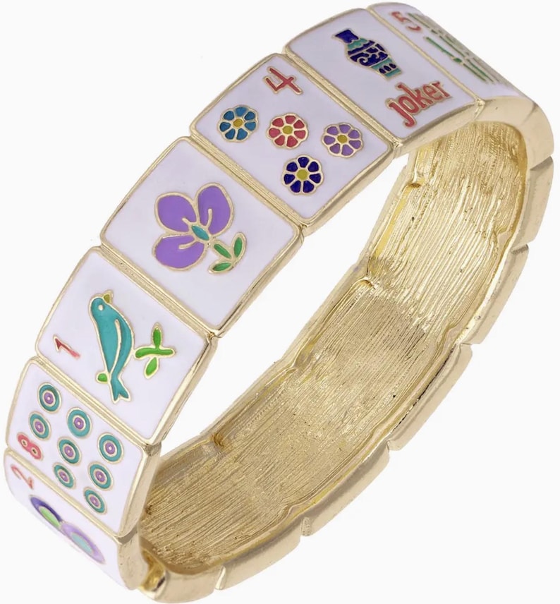 May include: A gold-toned bracelet featuring white rectangular tiles with colorful Mahjong symbols and a "Joker" tile. The tiles display various floral and bird designs, and the bracelet has a textured, brushed metal finish.