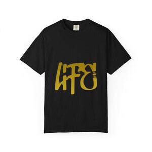 May include: Black t-shirt with a gold-colored graphic that reads "LIFE" in a stylized font. The shirt is a basic crew neck style, with short sleeves. The fabric appears to be a soft cotton blend.