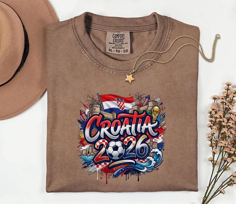 a brown t-shirt with a graphic design depicting the word "Croatia" surrounded by various elements such as a soccer ball, flags, and buildings.