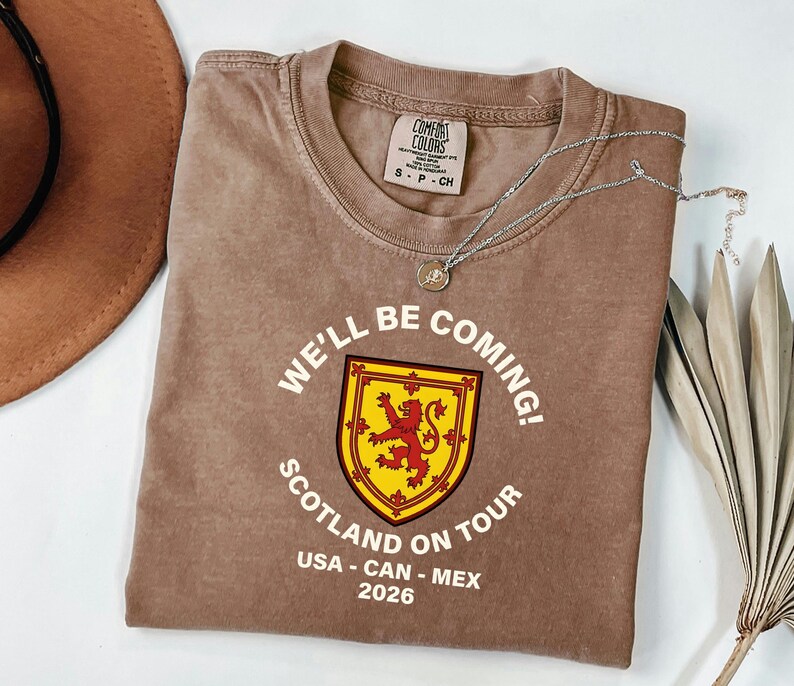 a brown t-shirt with a graphic design, a necklace, a hat, and some leaves on a white background.