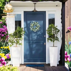 May include: A navy blue front door with a wreath, flanked by two white planters with small trees. The door is part of a white house with a wooden porch. The image includes the text "Little Nest Home" and "Home Decor & Accents".