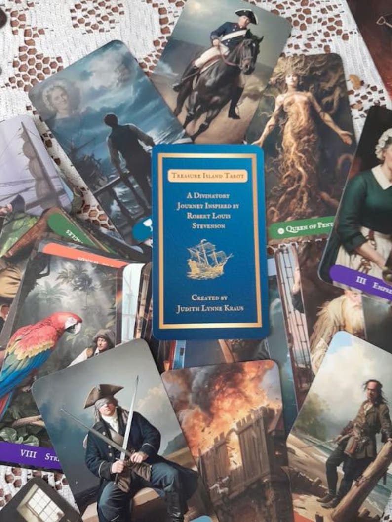 K&ouml;nnte beinhalten: Ein Satz Tarotkarten mit Illustrationen von Piraten, Schiffen und historischen Figuren. Die zentrale Karte ist blau mit goldener Schrift und tr&auml;gt die Aufschrift "Treasure Island Tarot" und "A Divinatory Journey Inspired by Robert Louis Stevenson."