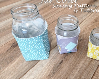 May include: Three glass jars with fabric covers. The covers feature different patterns: blue polka dots, purple with shapes, and yellow floral. The text "Jar Cover Sewing Pattern & Tutorial" is at the top.