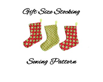 May include: Three Christmas stockings in a row, each with a different pattern. The stockings are red and green, with patterns including polka dots and diamond shapes. The text "Gift Size Stocking Sewing Pattern" is above and below the stockings.
