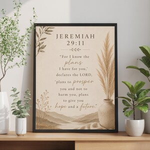 May include: A framed wall art print featuring the Bible verse Jeremiah 29:11 in dark brown text on a beige background. The design includes illustrations of pampas grass in a vase, leafy branches, and a landscape of rolling hills at the bottom.