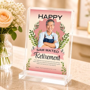 May include: A clear acrylic retirement photo frame with the words "HAPPY" and "Retirement" in black. The frame features a photo of a smiling man and the name "SAM MATEO". Green leaves and a pink banner decorate the frame.